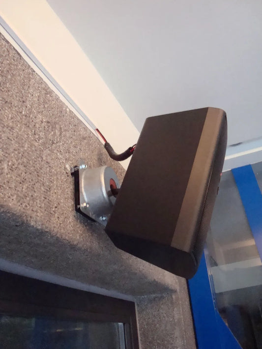 Wall-mounted black speaker with silver bracket.