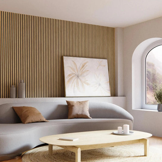 Interior of a room with light wood slat wall, gray couch with pillows, coffee table with candles and a book, and framed floral art.